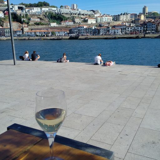 Photograph with a glass of white win on a table with Porto's river, other side of the river, and blue skies